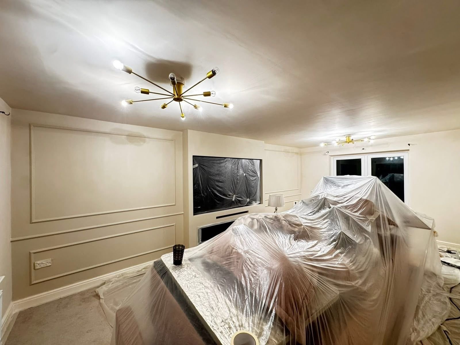 Living room with picture-frame wall panelling and gold ceiling light, covered for painting